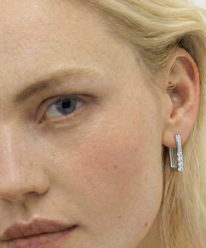 Close-up of a person wearing a silver hoop earring with a small gemstone.