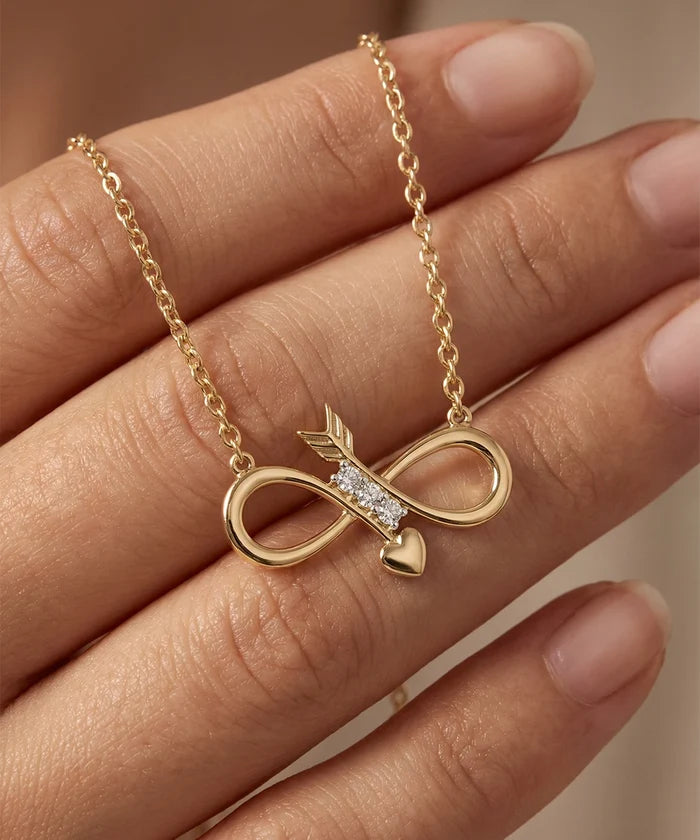Gold necklace with an infinity symbol and heart pendant on a hand against a neutral background