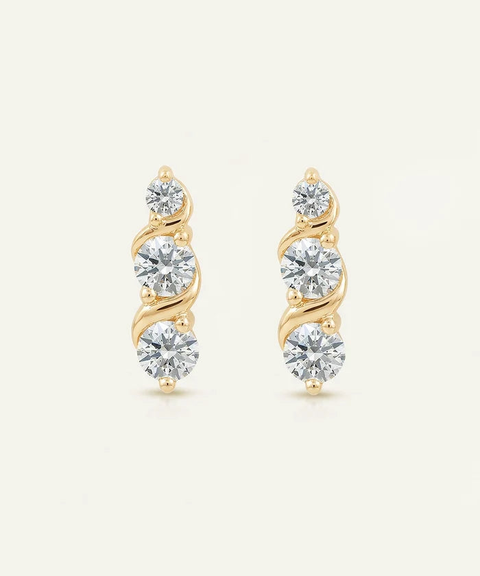 Pair of gold earrings with clear gemstones on a light beige background