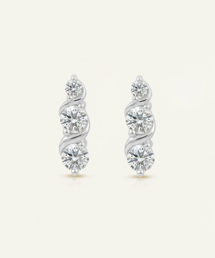 Pair of silver earrings with diamond-like stones on a light beige background