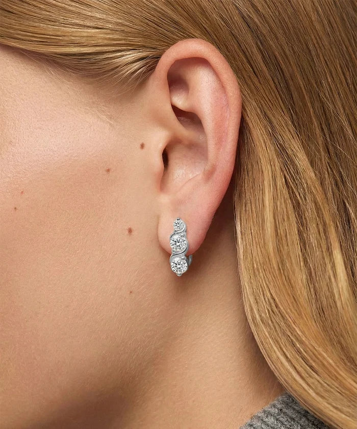 Close-up of an ear wearing a silver earring with three diamonds, blonde hair partially visible.