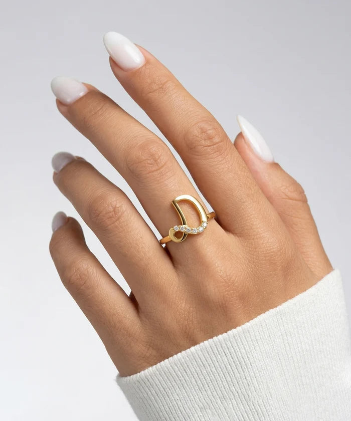Gold ring on a hand with white nail polish against a light gray background