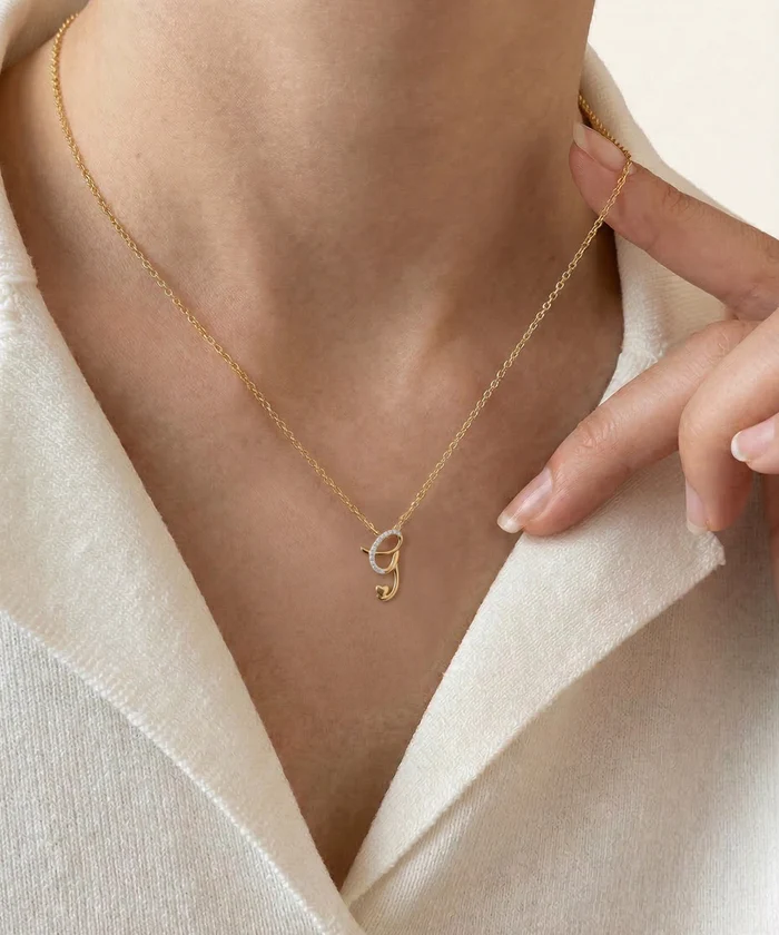 Gold necklace with a letter 'G' pendant worn by a person against a neutral background