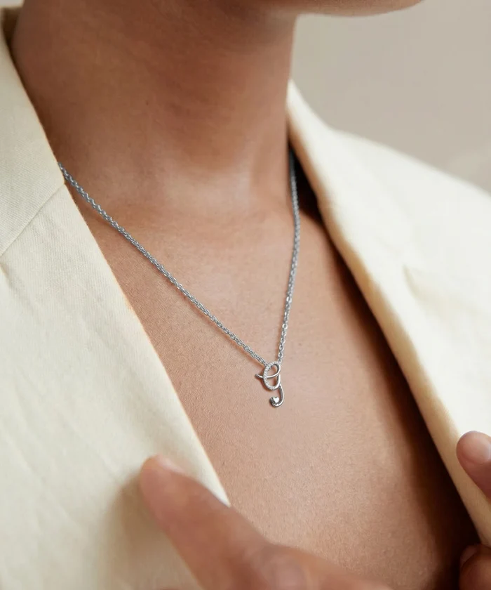 Silver necklace with a small pendant worn by a person in a cream blazer.