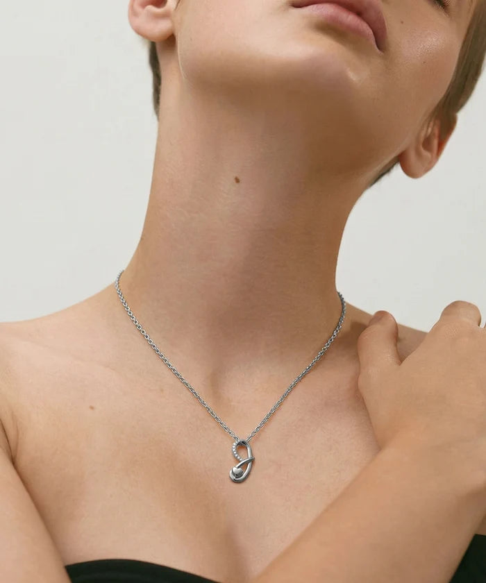 Person wearing a silver necklace with a unique pendant on a neutral background