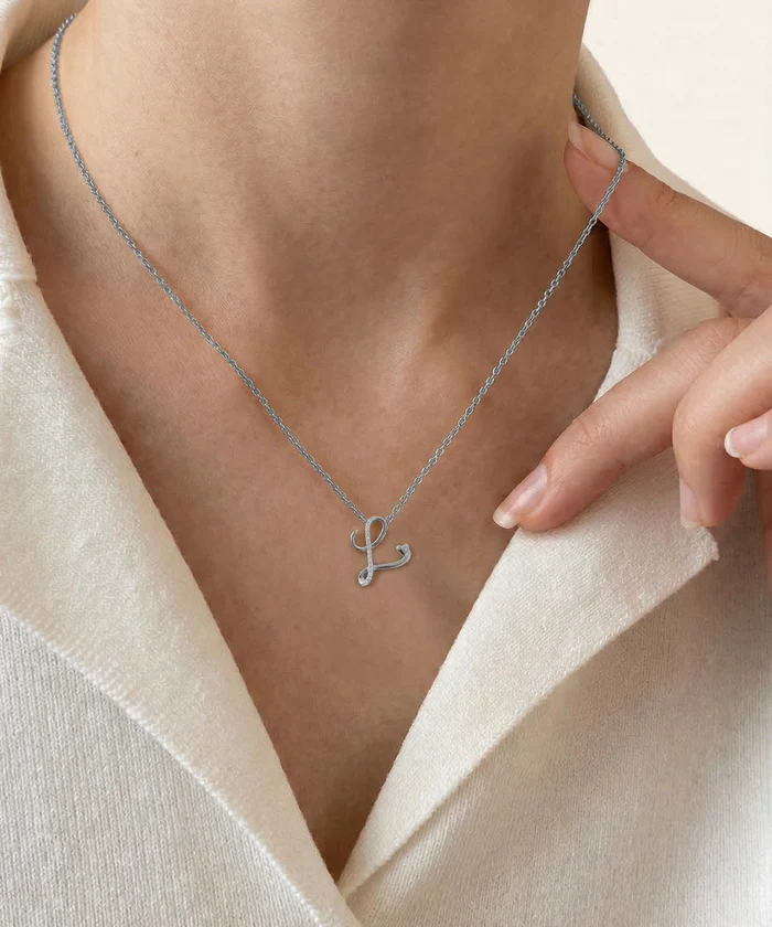 Silver necklace with a letter 'R' pendant worn by a person in a light-colored garment.