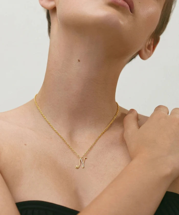 Gold necklace with a letter 'N' pendant on a person wearing a black top.