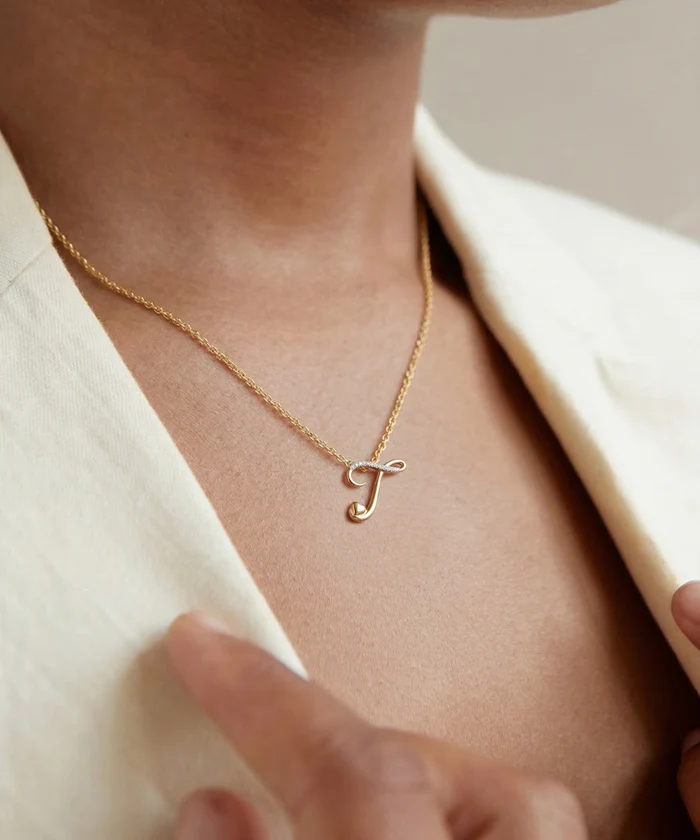 Gold necklace with a letter 'J' pendant on a person wearing a beige outfit.