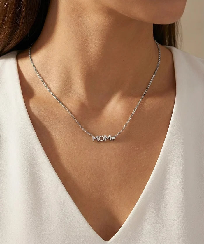 Silver 'MOM' necklace worn by a person in a white top.