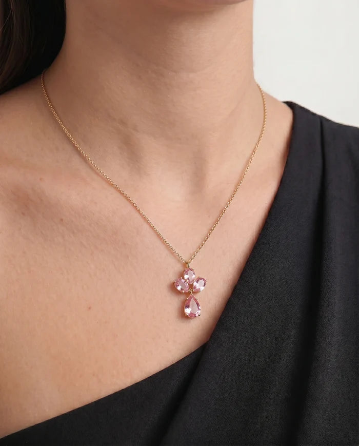 A close-up of a model wearing a delicate gold chain necklace with a small pink gemstone pendant.
