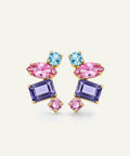 A pair of gold-plated statement earrings featuring marquise-cut pink crystals, rectangular purple crystals, and round light blue crystals, set against a light cream background.