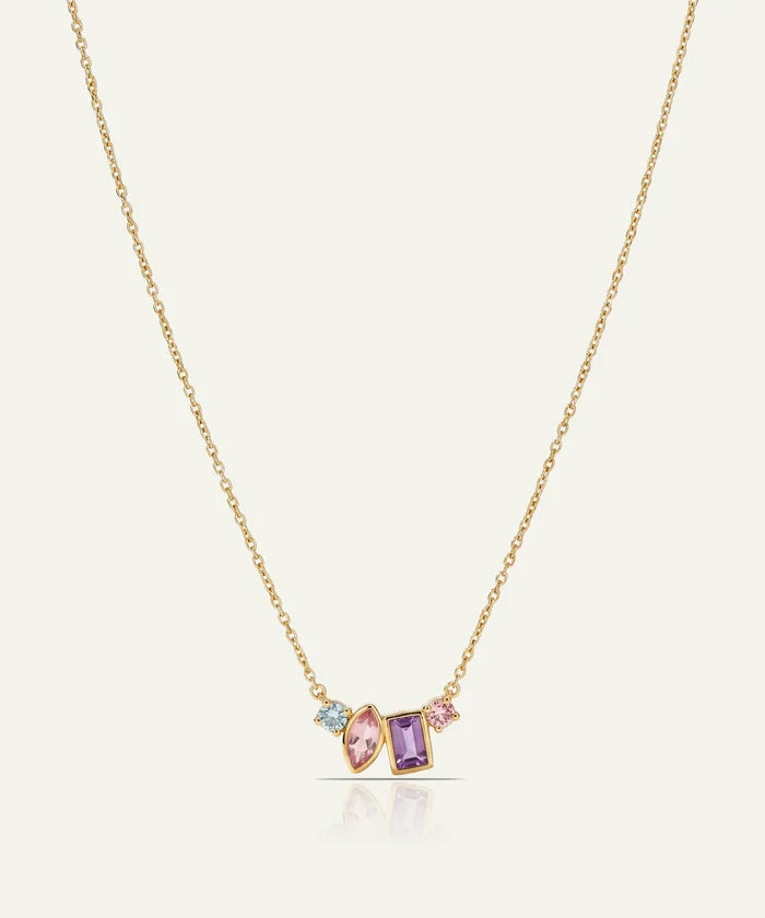 A delicate gold chain necklace featuring a small cluster pendant with a marquise-cut pink gemstone, a rectangular purple gemstone, and a tiny light blue gemstone, set against a light cream background.