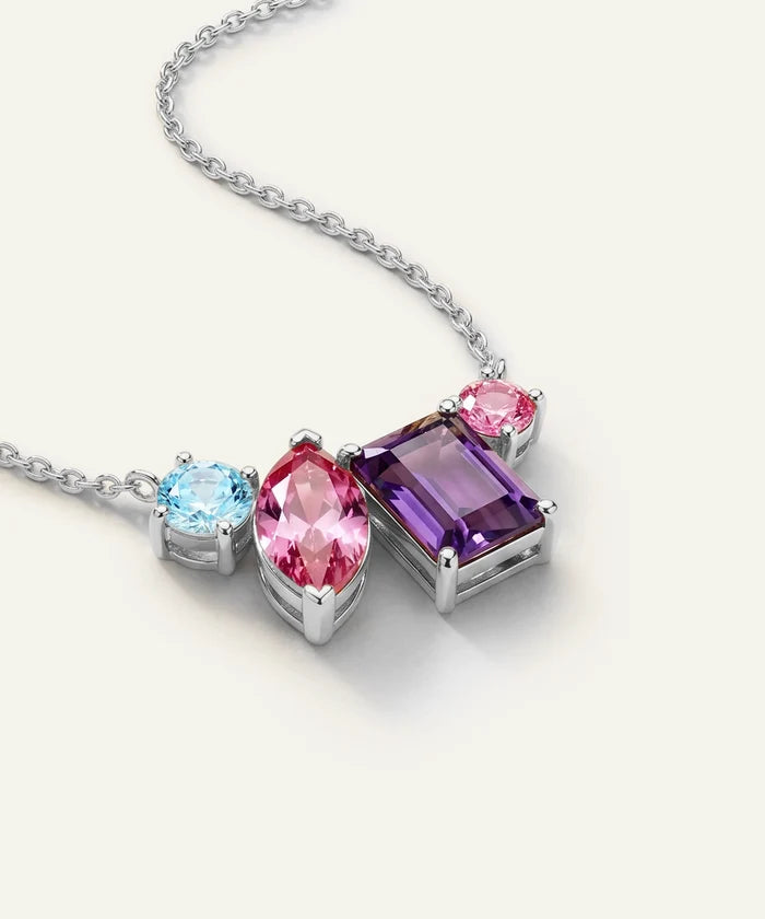 A silver-tone pendant necklace featuring three colored gemstones: a large rectangular purple amethyst, a marquise-cut pink tourmaline, and a round light blue cubic zirconia, displayed on a clean off-white background.