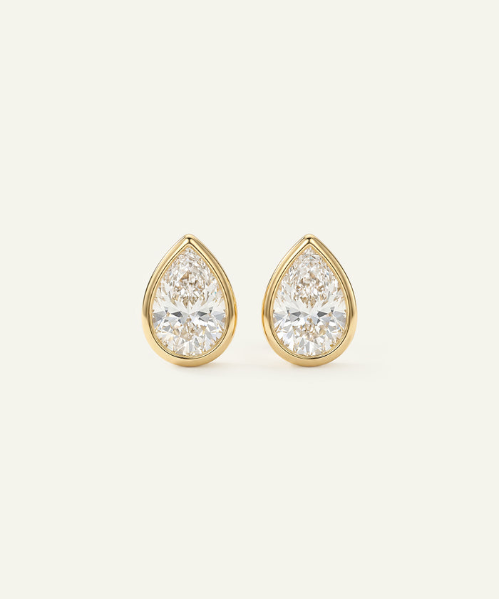 Gold teardrop earrings with clear gemstones on a light beige background