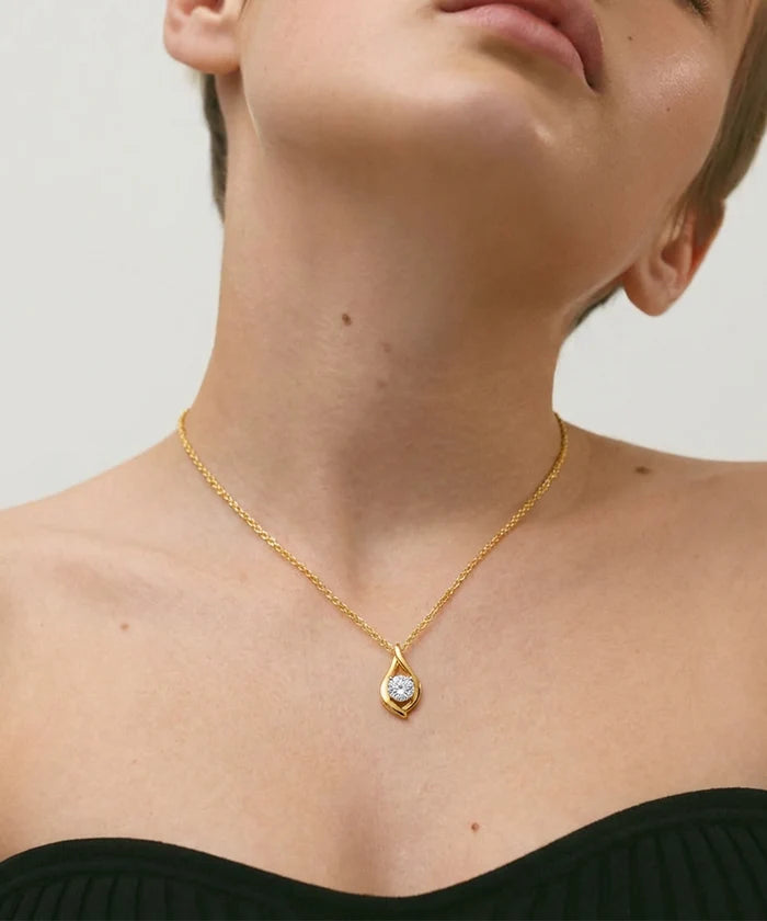 Gold necklace with a diamond pendant worn by a person against a neutral background
