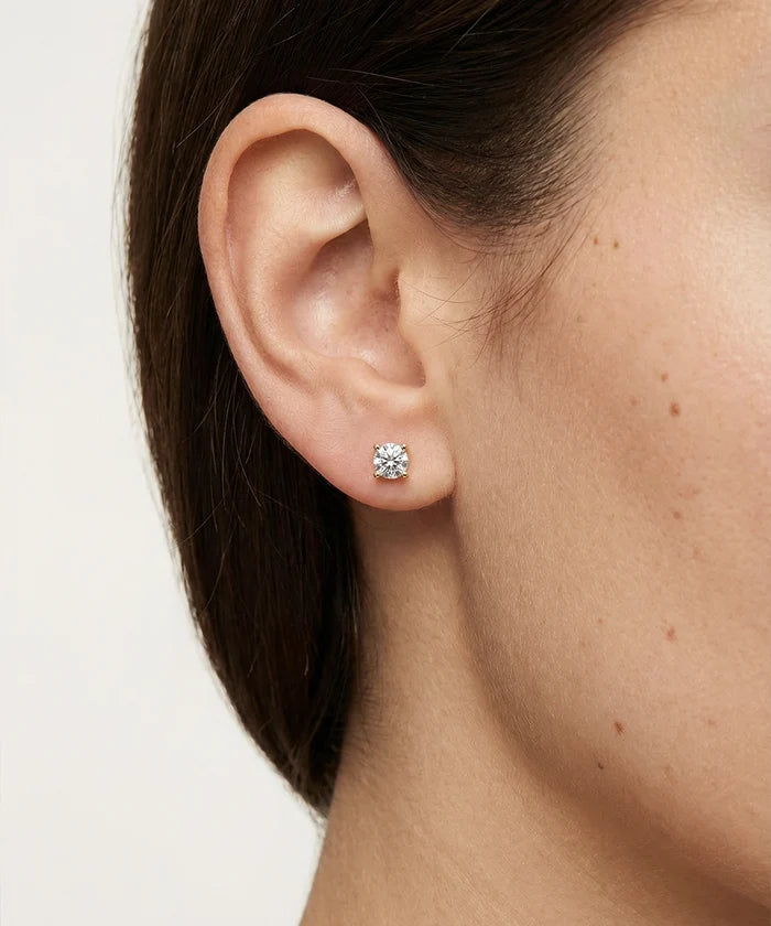 Close-up of an ear wearing a diamond stud earring on a plain background