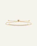 A delicate gold-tone adjustable bracelet featuring a curved bar set with small clear stones, displayed on a light cream background.