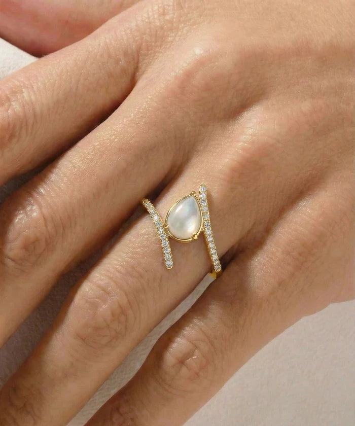 Gold ring with a central gemstone on a hand against a neutral background