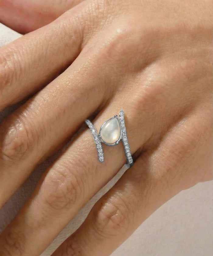 Silver ring with a central gemstone on a hand against a neutral background