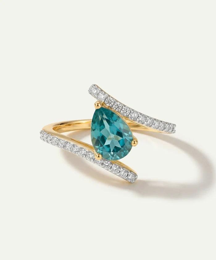 Gold ring with a pear-shaped blue gemstone and diamond accents on a white background