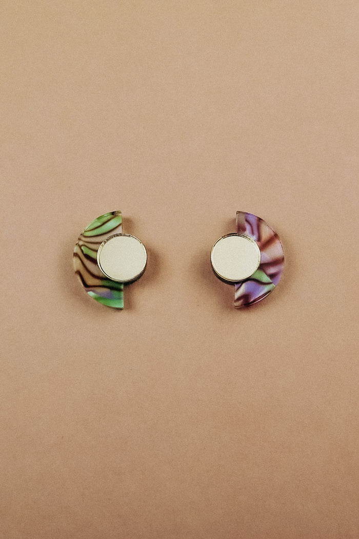 Minimalist Geometric Stud Earrings featuring two semicircular designs with round silver centers: the left earring shows a green and brown marbled pattern, while the right displays pink and purple, set against a plain beige background.