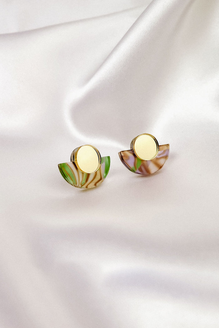 Minimalist Geometric Stud Earrings featuring gold centers and semi-circular marbled green, brown, and purple acrylic accents, displayed on smooth white satin fabric.
