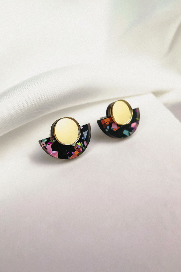 Minimalist Geometric Stud Earrings featuring gold circular tops and black semicircular bottoms with colorful, confetti-like patterns. These lightweight, hypoallergenic earrings are displayed on a white fabric background.
