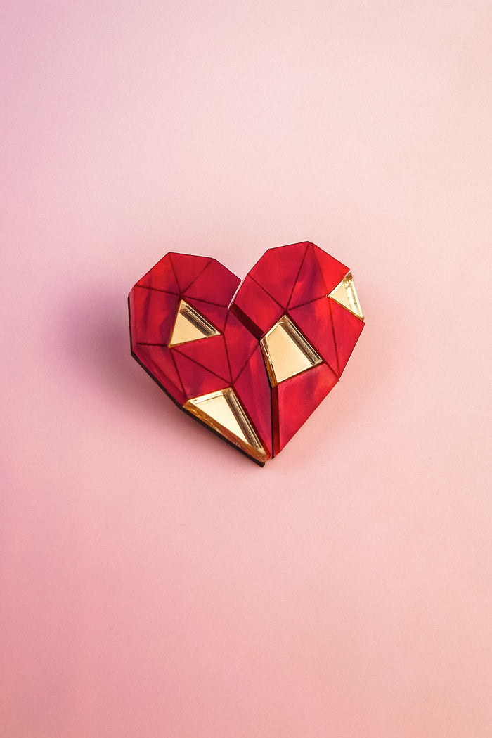 A geometric, origami-style red heart with gold triangular accents sits on a soft pink background—perfect as romantic gift or inspiration for handcrafted pins.