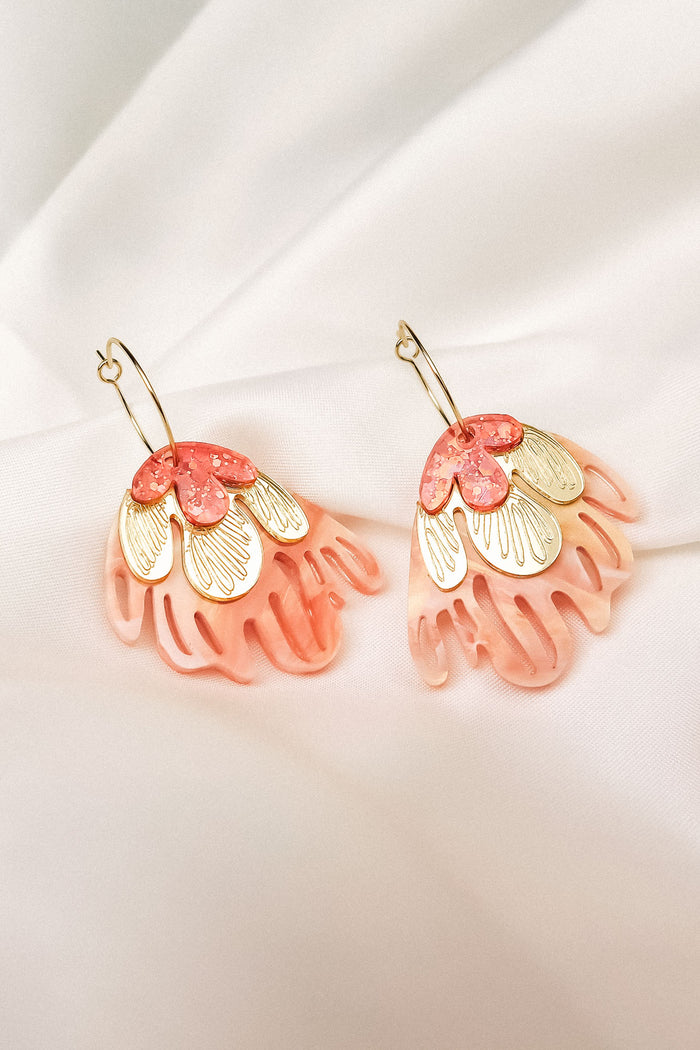 A pair of decorative Organic Floral Hoops featuring pink translucent petal-like acrylic flowers and gold accents, displayed on a soft white fabric background.