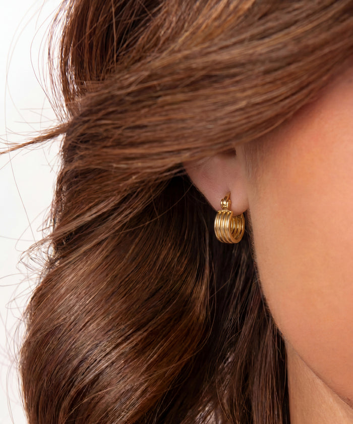 Gold hoop earrings worn by a person with brown hair.