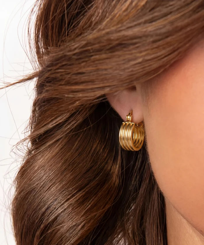 Close-up of a person wearing gold hoop earrings with hair partially covering the face.