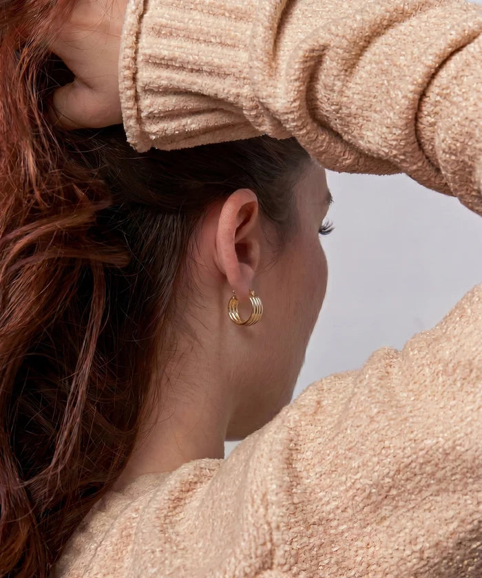 Close-up of a person wearing gold hoop earrings with a neutral background