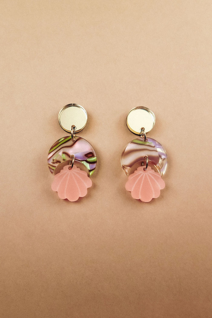 Handmade gold and marbled pink Seashell Earrings with circular tops, lightweight translucent marbled middles, and pink shell-shaped pendants, displayed on a light beige background.