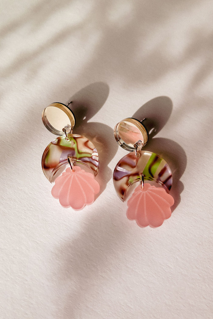 A pair of lightweight, handmade Seashell Earrings featuring round mirrored studs, marbled pink and brown circles, and pink shell-shaped pendants, displayed on a light surface with soft shadows.