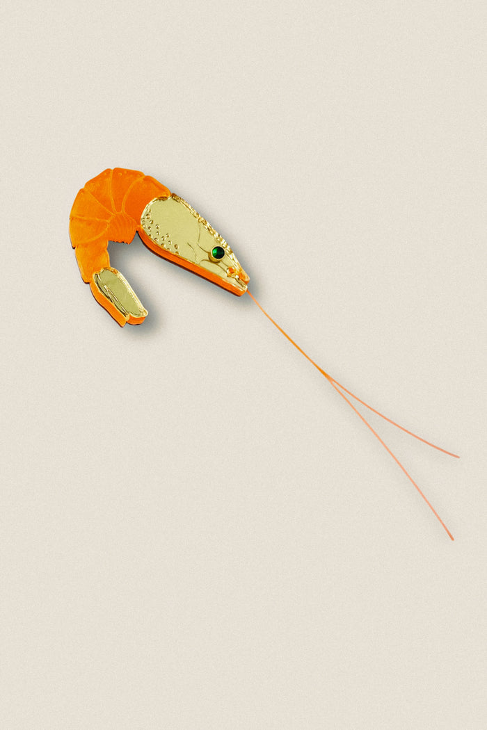 A Shrimp Pin accessory designed to resemble a shrimp, with an orange segmented body and detailed gold head, featuring green and black accent stones and long, thin orange antennae—perfect for adding wardrobe charm against any outfit.