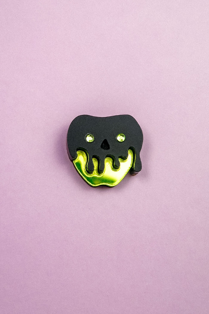 A pin shaped like an apple with a shiny yellow bottom and a black, drippy skull design on top, this Poisoned Apple Badge is perfect for Halloween lovers. Set against a plain light purple background—grab yours now, as stock is limited!.