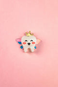 A smiling cartoon tooth with rosy cheeks, wings, and a gold crown sits centered on a pink background, making this handcrafted Tooth Fairy Pin perfect for celebrating childhood milestones.