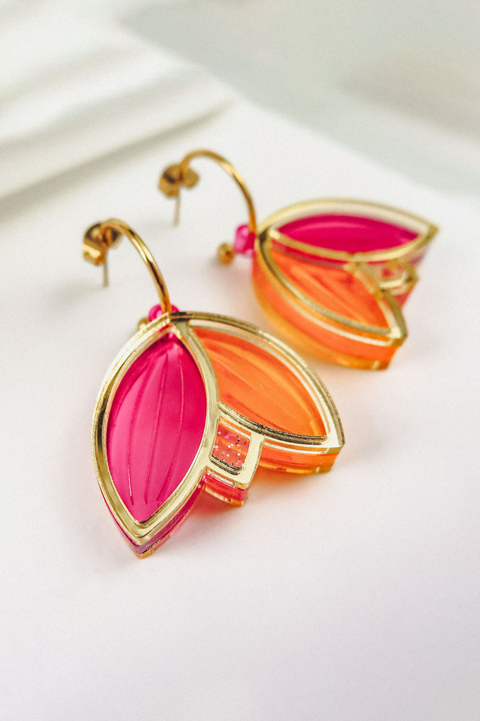 A pair of Tulip Huggie Earrings with artisan craftsmanship, featuring three leaf-shaped charms in vibrant colors—translucent pink and orange outlined in gold—displayed on a white surface.