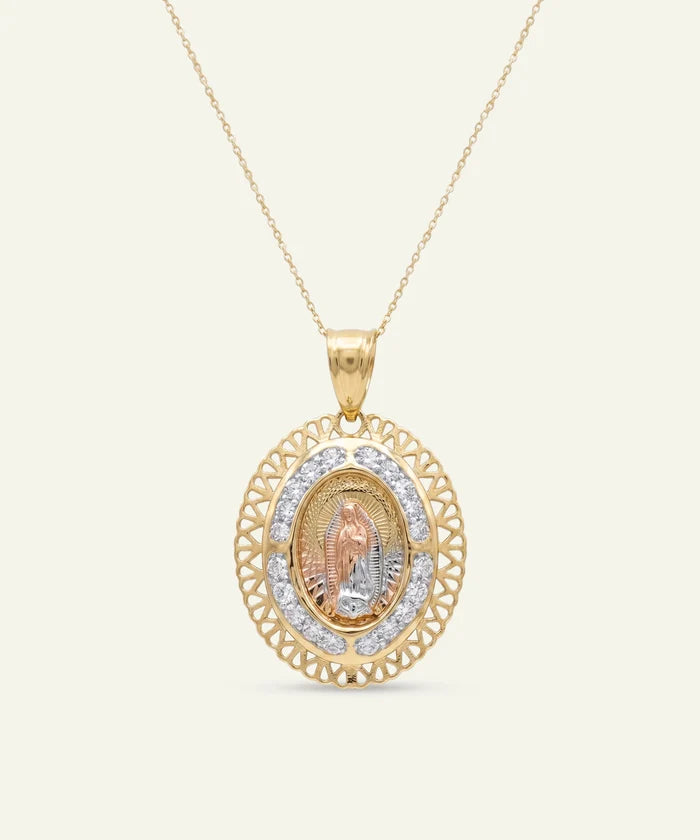 Gold necklace featuring an oval pendant with an intricate filigree outer border and a pave diamond halo. The center showcases a detailed, three-dimensional relief figure of Our Lady of Guadalupe in tri-color gold, suspended on a delicate gold chain.